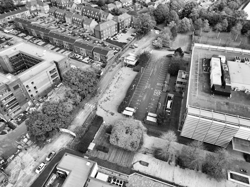 A black-and-white aerial photograph of an urban garden space situated between modern apartment buildings and residential houses in Noel Park. The garden features a large paved area with numerous marke